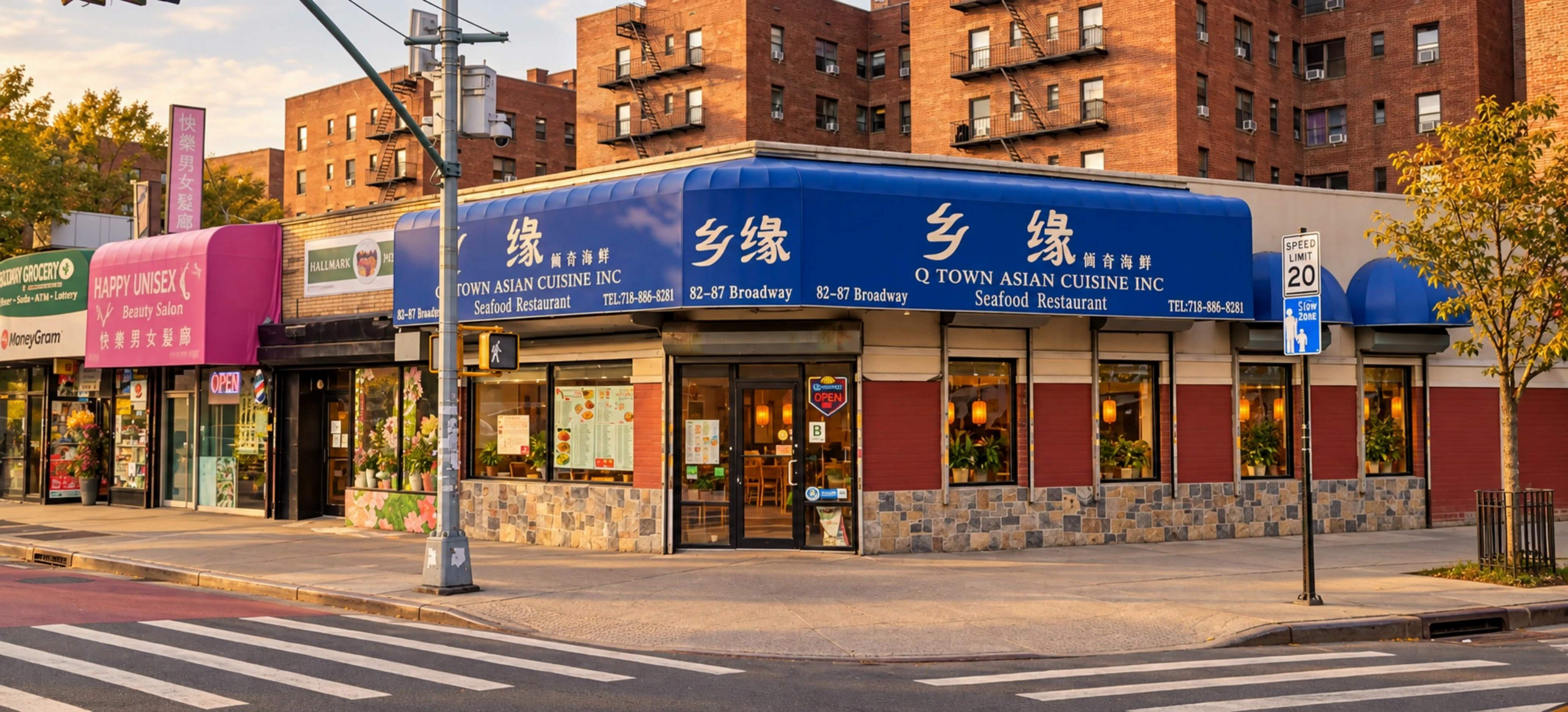 Corner storefront of Q Town Asian Cuisine with a blue awning, red brick and stone base, lanterns in the windows and the entrance door on the corner.