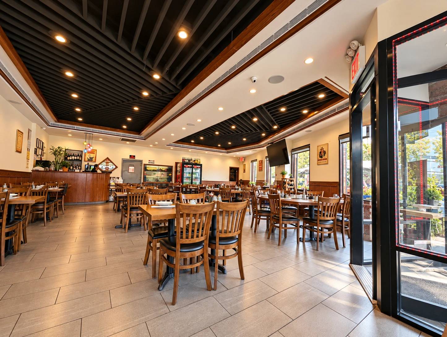 Dining room seen from the entrance: wood tables and chairs, cream walls, a dark slatted ceiling with spotlights, the counter and drinks fridge at the back.